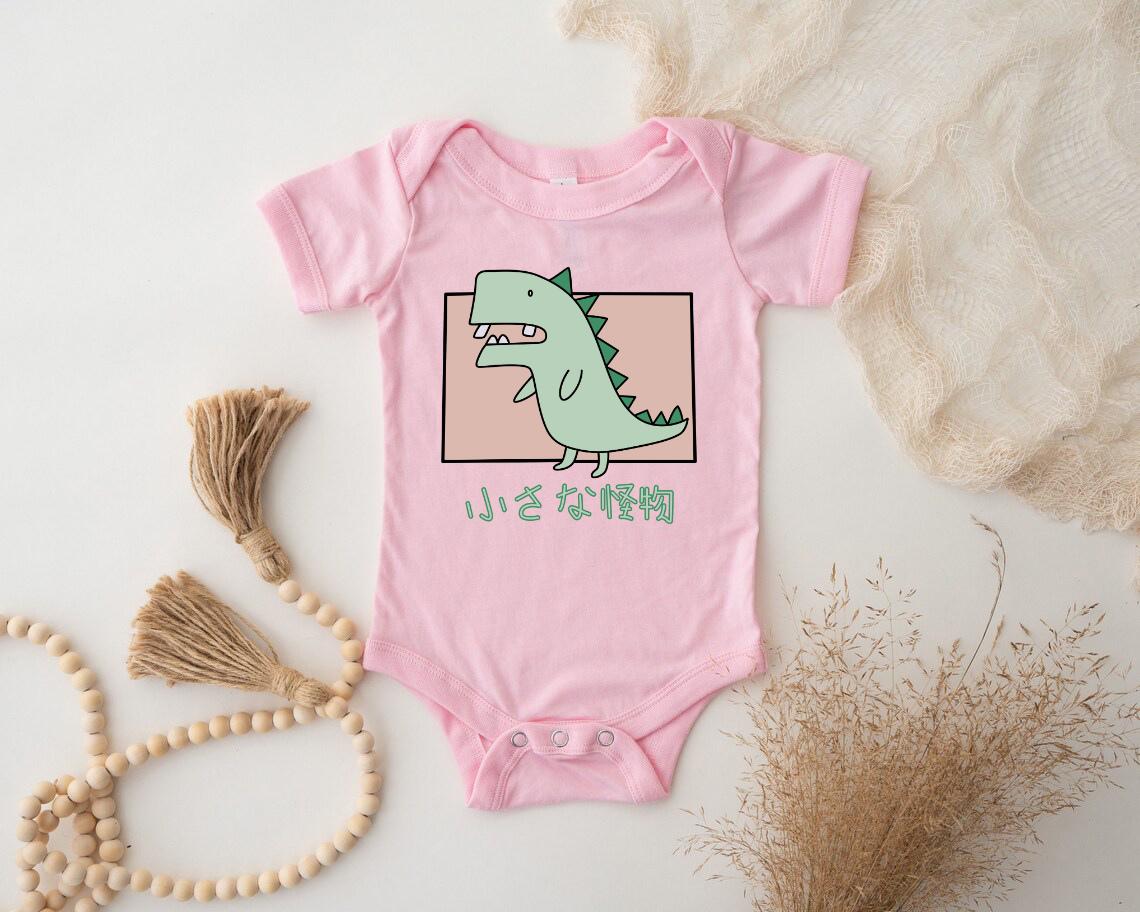 a pink baby bodysuit with a green dinosaur on it