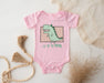 a pink baby bodysuit with a green dinosaur on it
