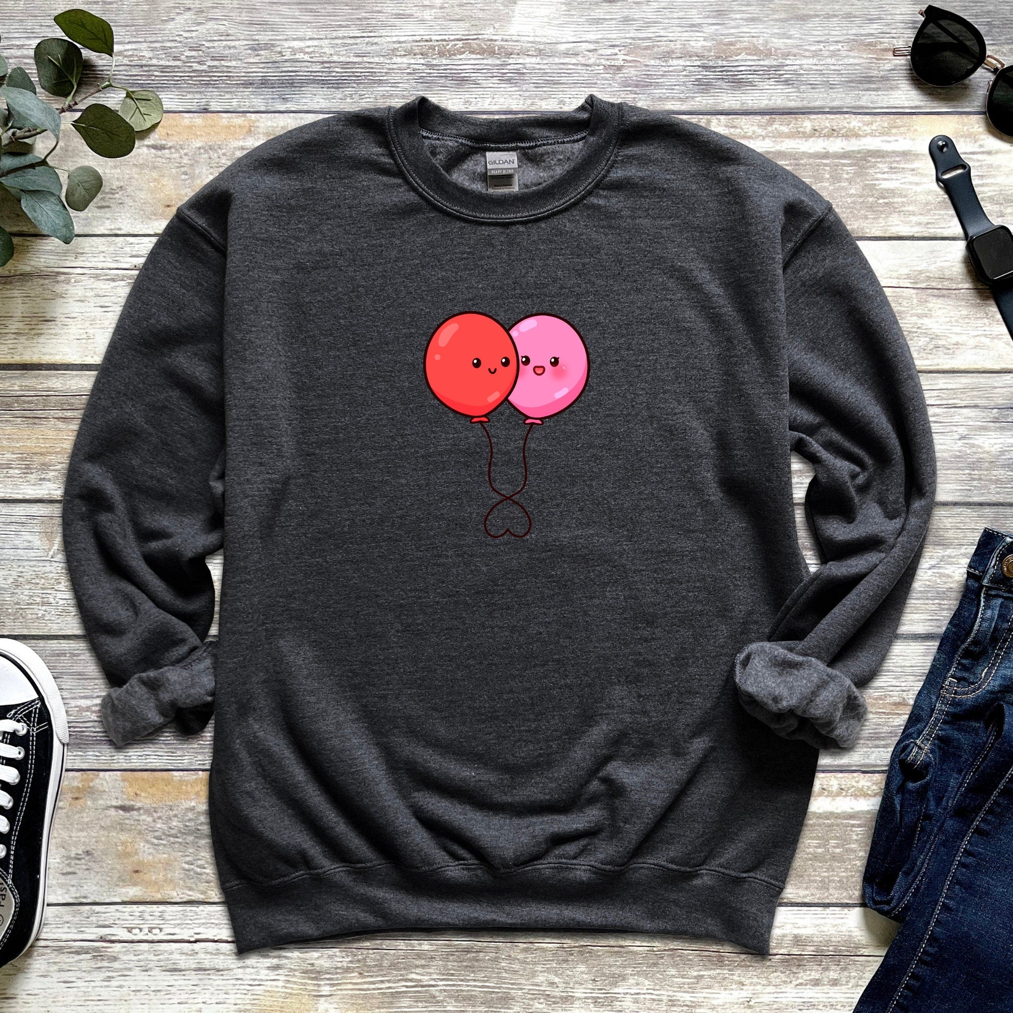 a sweater with two balloons on it next to a pair of jeans